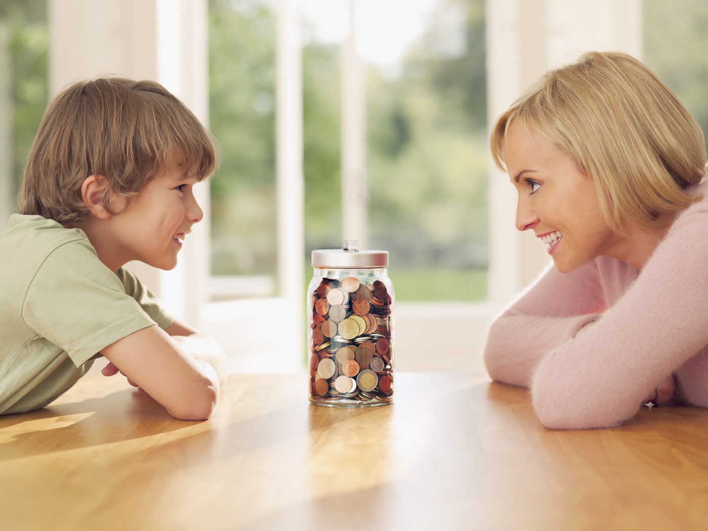 Mutter und Sohn schauen lächelnd auf ein Sparglas voller Münzen